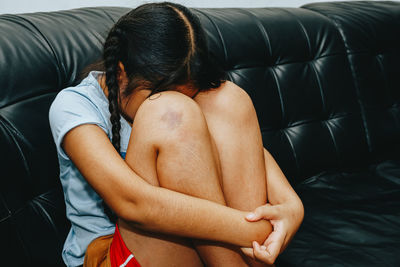Girl hugging knees sitting on sofa at home