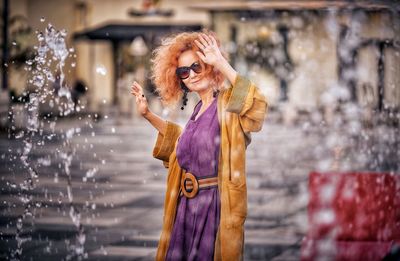 Portrait of woman standing amidst fountain outdoors