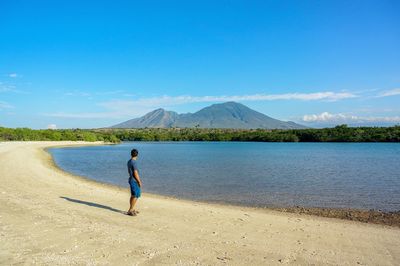 Rear view of man on lake against blue sky