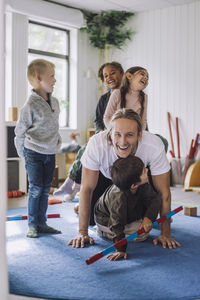 Happy male teacher enjoying with male and female students in day care center