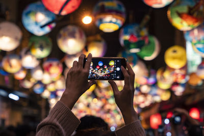 Man photographing illuminated mobile phone at night