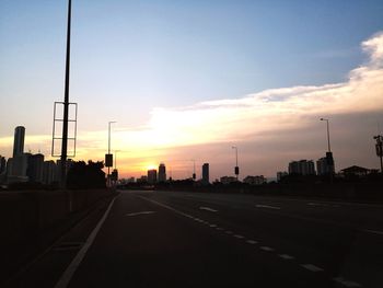 Road by city against sky during sunset
