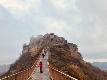 Rear view of woman standing on cliff against cloudy sky