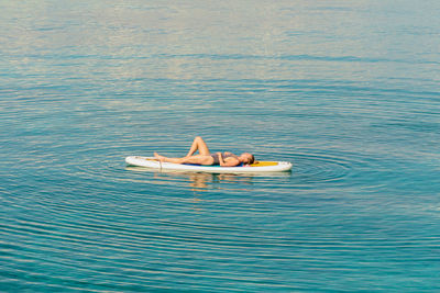 Full length of woman lying down on surfboard in sea