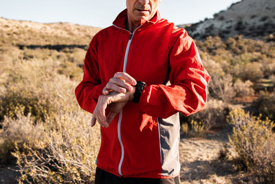 Concentrated middle aged male athlete in activewear checking time on smartwatch while standing in hilly terrain after workout