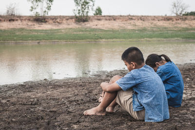 Rear view of men sitting by lake