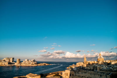 Buildings by sea against blue sky