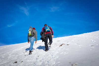 Mountain hikers climb to the snowy peak, blue sky in the background.