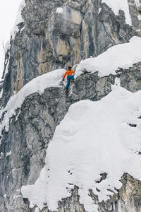 Low angle view of woman climbing on snowcapped mountains during winter