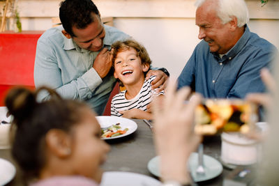 Senior woman photographing happy family at dining table during lunch