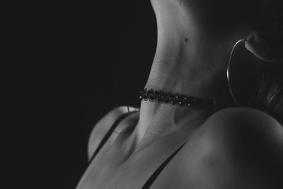 Close-up of woman wearing choker against black background