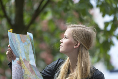 Woman holding map while looking away in city