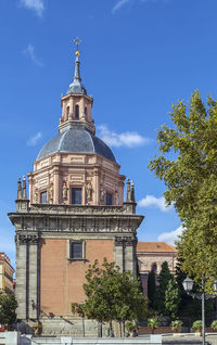 Low angle view of trees and buildings against blue sky