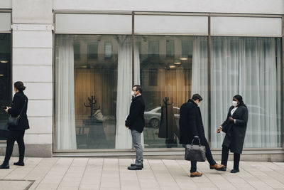 Business people greeting with foot tap while male and female colleagues standing on footpath during covid-19