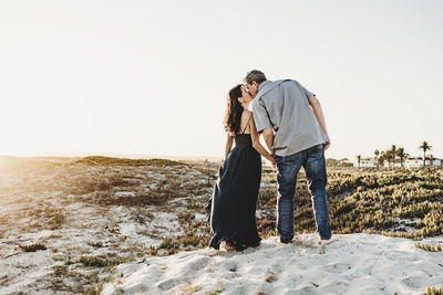 Romantic mid-40's couple kissing while standing on sand dune at beach