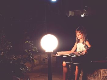 Full length of woman sitting in illuminated lamp