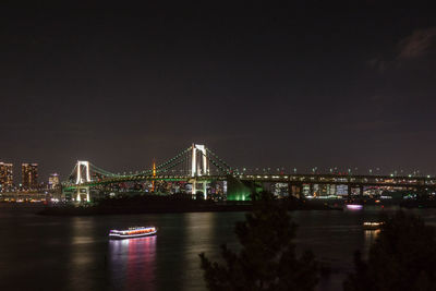 Illuminated rainbow bridge over sea against clear sky at night