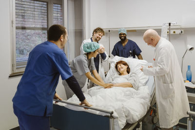 Smiling healthcare workers cheering while standing around senior female patient at hospital