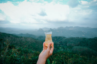 Midsection of person holding drink against mountain range