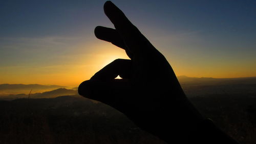Close-up of silhouette hand against scenic sky