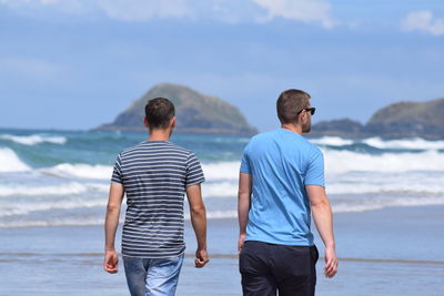 Rear view of men standing at beach against sky