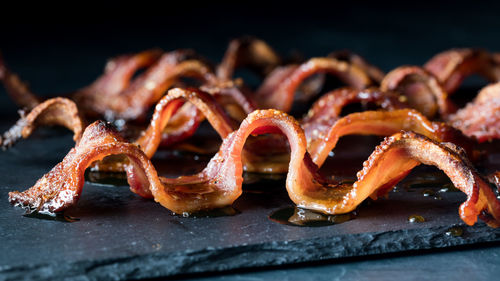 Wavy strips of crispy maple pepper bacon on a black slate board.