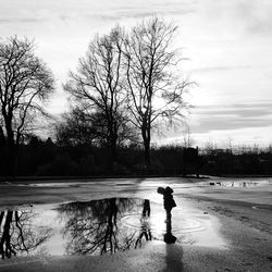 Girl standing in puddle against bare trees