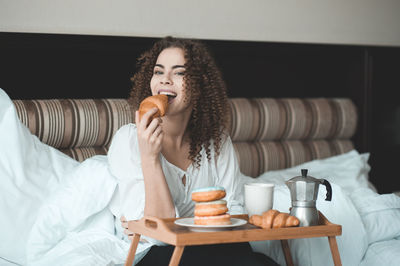 Portrait of smiling woman eating croissant at home