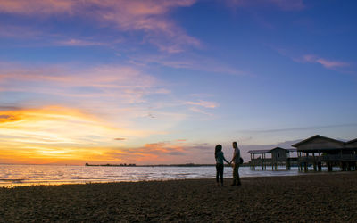 Silhouette of couple on beach against sky during sunset