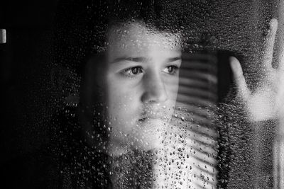 Close-up portrait of wet boy looking through window