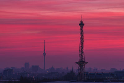Communications tower in city against dramatic sky at sunset
