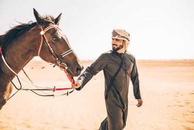 Man with horse walking at desert against clear sky