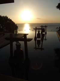 Silhouette people in swimming pool by sea against sky during sunset