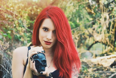 Close-up portrait of young woman holding black human skull against plants
