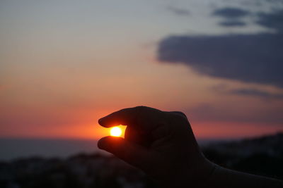 Optical illusion of hand against sky during sunset