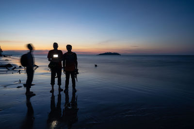 People holding camera while standing at beach during sunset