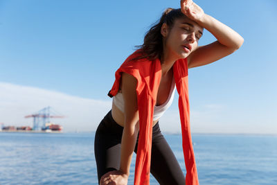 Tired young woman standing against sea