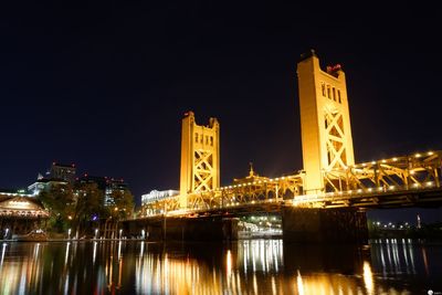 Illuminated buildings by river against sky at night