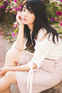 Portrait of young woman sitting against flowering plants