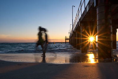 Man walking on beach against sky during sunset