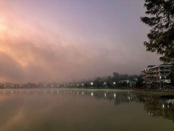 Scenic view of lake by buildings against sky at sunset