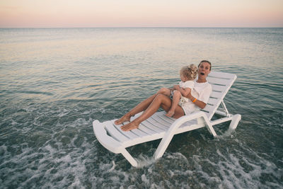 Surprised mother and daughter on beach lounger as waves approach