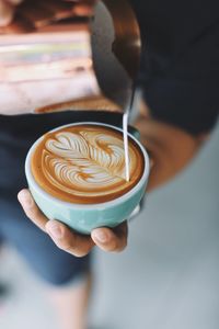 Midsection of person pouring milk in coffee