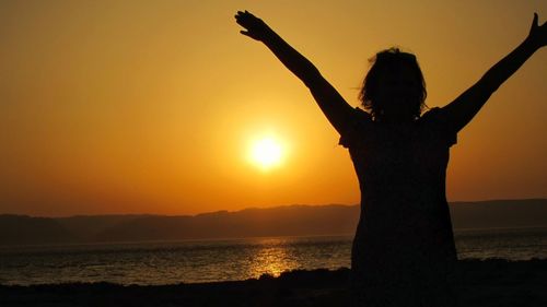 Silhouette woman standing at beach during sunset