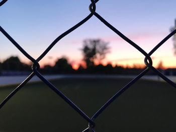 Close-up of chainlink fence against sky during sunset