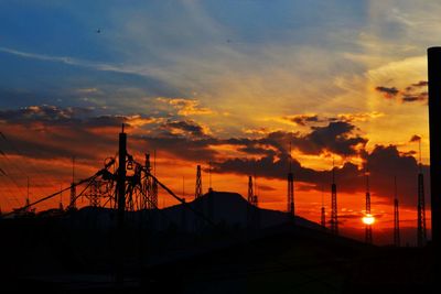 Silhouette of electricity tower against dramatic sky during sunset