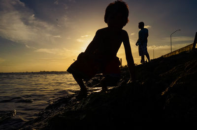 Silhouette people on beach against sky during sunset