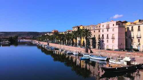 Boats moored on river by buildings against clear blue sky