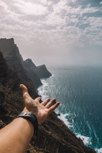 Close-up of hand by sea against sky