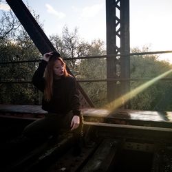 Woman sitting on railing against trees